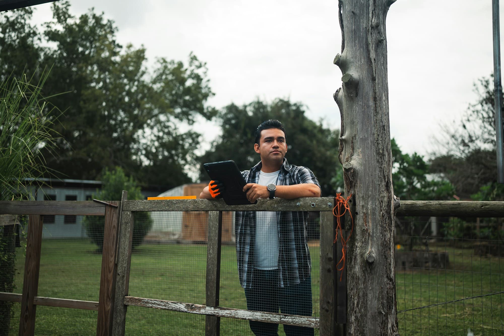 Técnico com tablet apoiado na cerca de uma propriedade rural